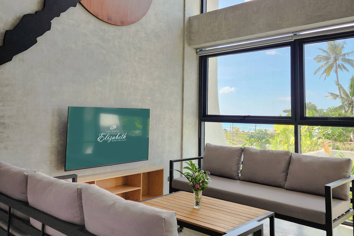 Une chambre d’hôtel moderne dotée d’une grande fenêtre, d’un téléviseur à écran plat, de deux canapés et d’un élément décoratif en bois sur le mur.