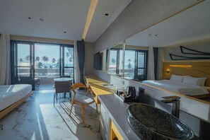 A hotel room with a bed, a desk, a chair, a large window with a view of palm trees, and a bathroom with a granite sink. - The Hotel Elizabeth Resort and Villas (San Vicente)