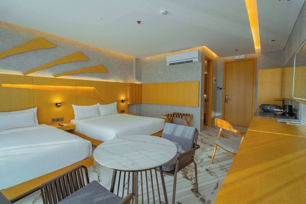 Une chambre d’hôtel avec deux lits, une table à manger ronde et un petit coin salon.