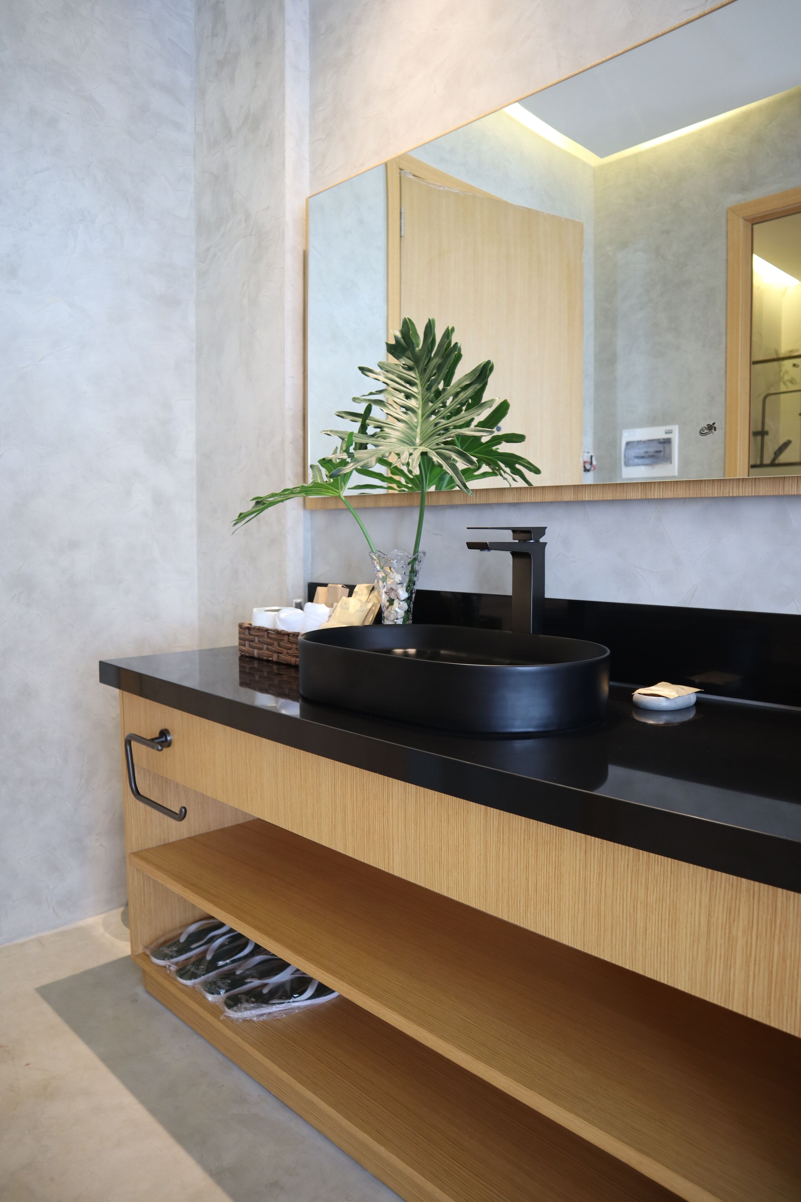 A modern bathroom with a black sink, a mirror, and a plant.