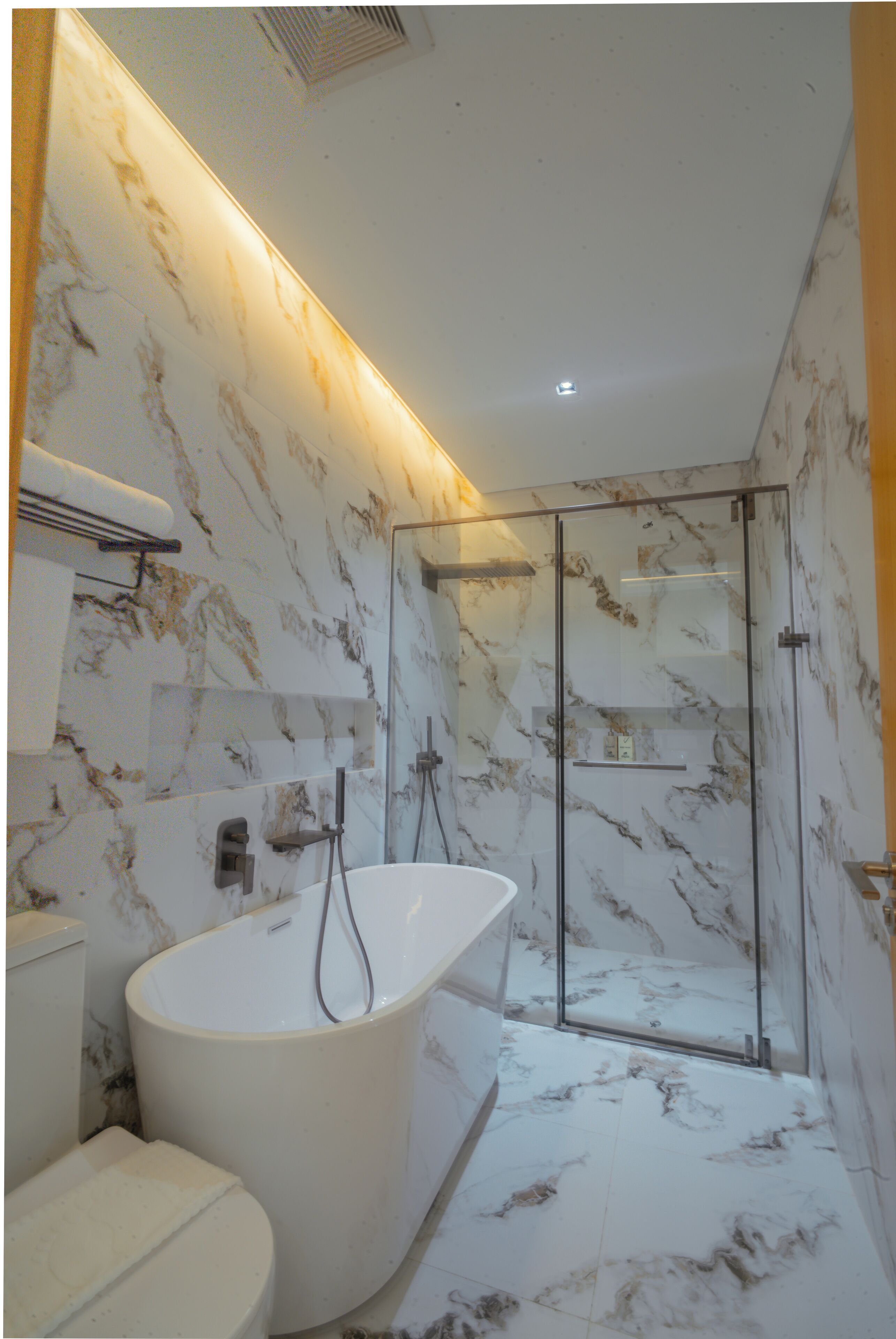 A modern bathroom with a freestanding bathtub, a glass-enclosed shower, and marble walls.
