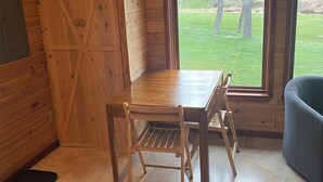 A wooden interior with a table and chairs, a large window, and a view of the outdoors. - Red Bluffs Lodge Upper Unit, located on the River, minutes from Devils Tower! (Hulett)