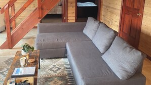 A cozy living room with a gray sectional sofa, a wooden staircase, and a rustic wooden wall. - Red Bluffs Lodge Upper Unit, located on the River, minutes from Devils Tower! (Hulett)