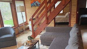 A cozy living room with a grey sofa, a wooden staircase, and a painting on the wall. - Red Bluffs Lodge Upper Unit, located on the River, minutes from Devils Tower! (Hulett)