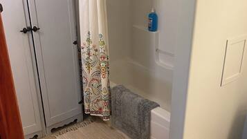 A bathroom with a shower, a toilet, a sink, a white cabinet, a patterned shower curtain, and a rug.