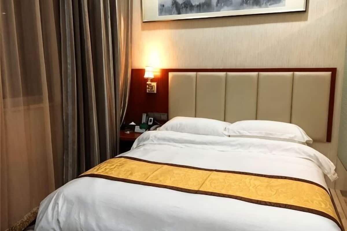 A hotel room with a bed, a nightstand, a lamp, and a painting on the wall.