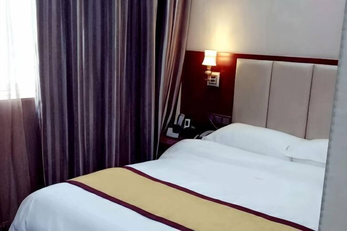 A hotel room with a bed, curtains, a nightstand, and a wall-mounted lamp.