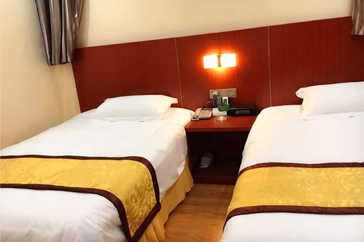 A hotel room with two beds, a nightstand with a lamp, a phone, and a small table with a bottle.
