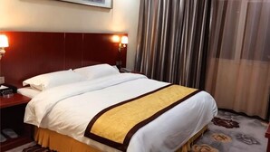 A hotel room with a large bed, two bedside tables, a nightstand, a framed picture on the wall, and a window with curtains.