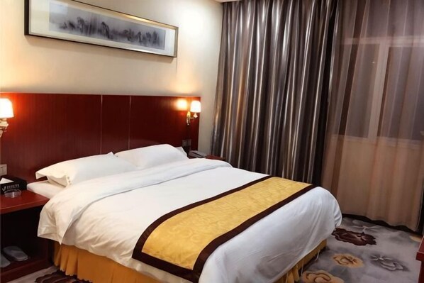 A hotel room with a large bed, two bedside tables, a nightstand, a framed picture on the wall, and a window with curtains. - Ganzhou Jinshawan Holiday Hotel (Lighting City Branch) (Ganzhou)