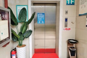 Un ascenseur agrémenté d’un tapis rouge, d’une plante en pot, d’un extincteur et d’un panneau indiquant les consignes de sécurité en cas d’urgence.