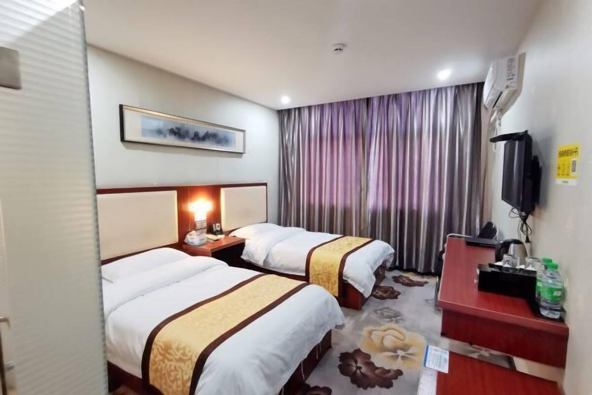A hotel room with two beds, a desk, a television, and a curtain.