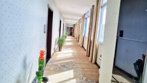 A hallway with patterned walls, a floral carpet, potted plants, and a door at the end.