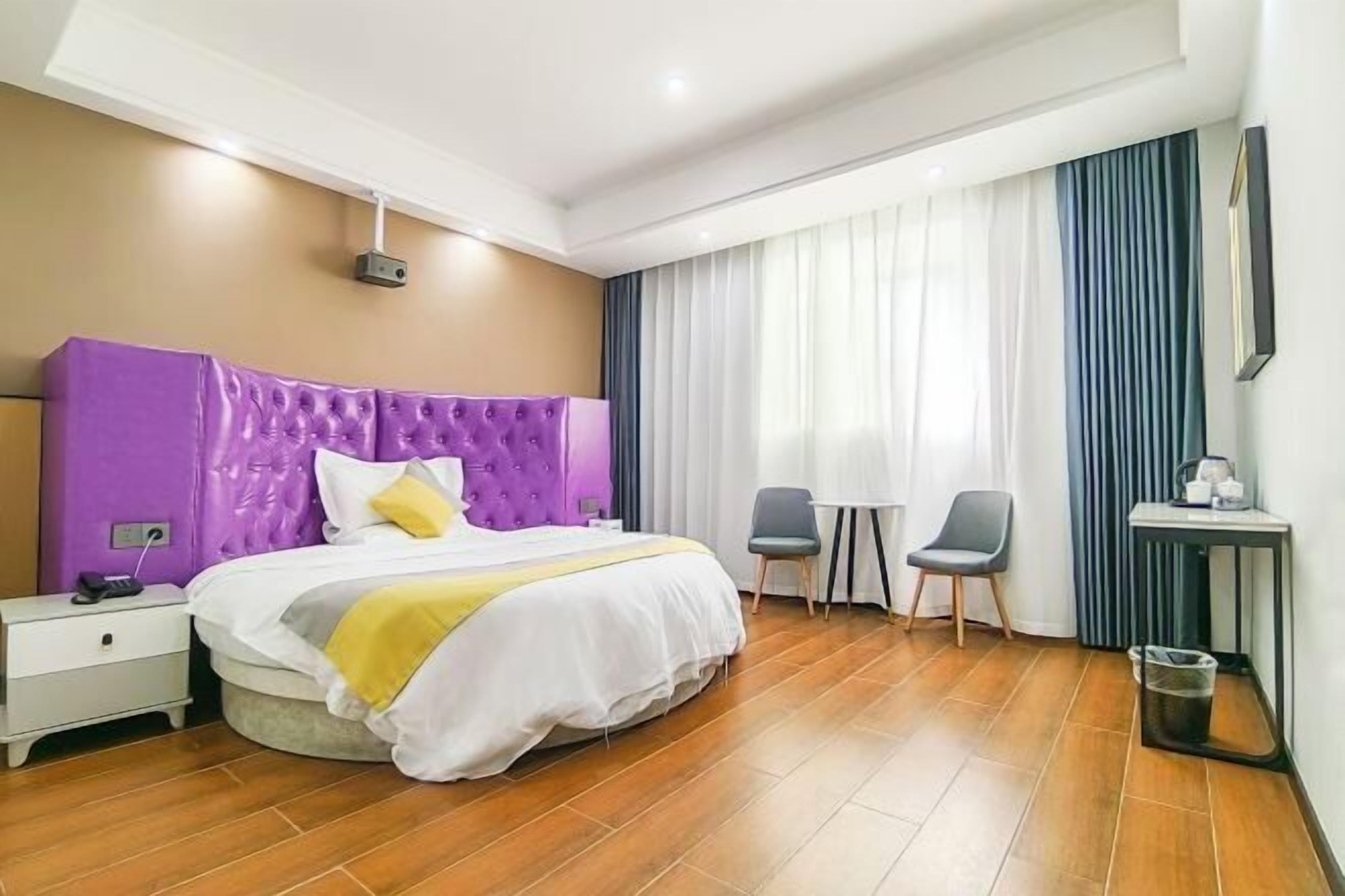 Ein Hotelzimmer mit einem großen Bett, einem kleinen Tisch, zwei Stühlen, einem Nachttisch und einer Mülleimer.