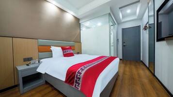A hotel room with a bed, bedside table, and a TV on the wall.