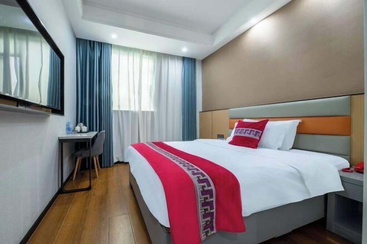A hotel room with a bed, a desk, a chair, a mirror, and a window with curtains.