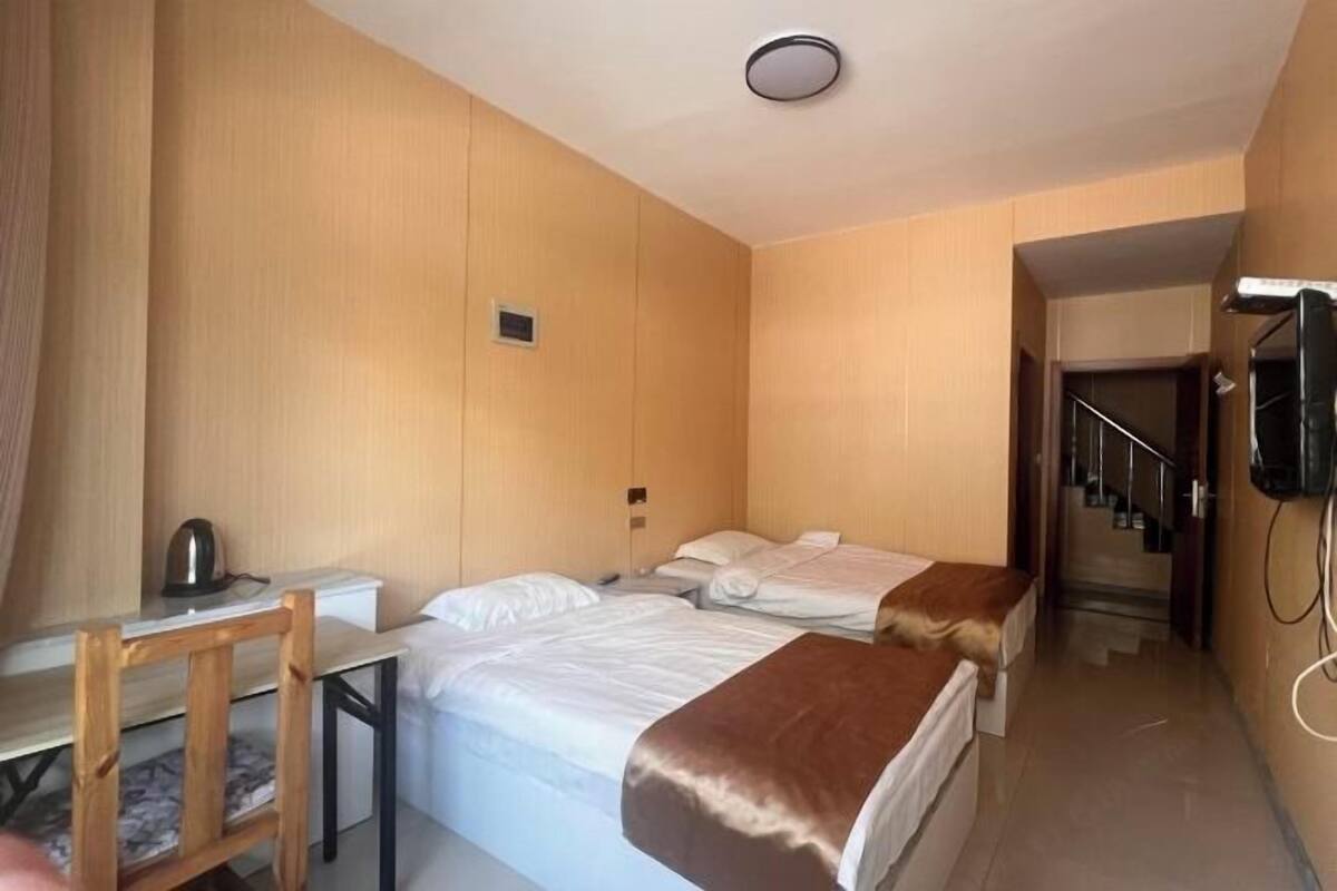 A hotel room with two beds, a desk with a chair, a telephone, and a staircase.