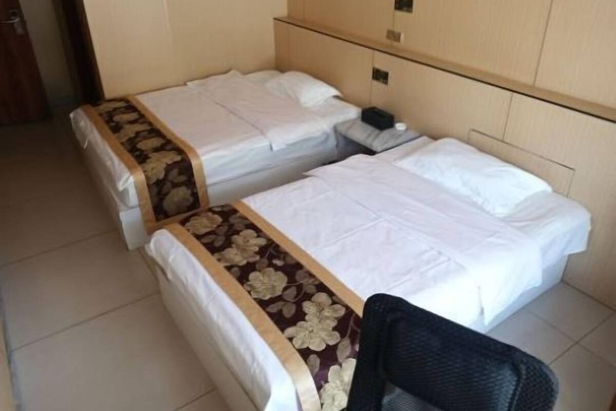A hotel room with two beds, a wooden headboard, a small desk, and a chair.
