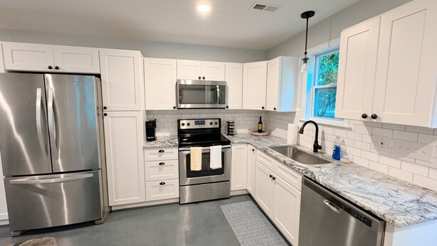 A modern kitchen with white cabinetry, stainless steel appliances, a marble countertop, and a built-in dishwasher. - Cozy North Raleigh Guest House - near RDU, DTR, + major Hospitals (Raleigh)