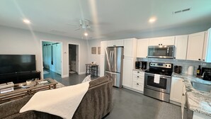A modern kitchen with stainless steel appliances, a dining area with a table and chairs, and a living room with a large TV and a sofa. - Cozy North Raleigh Guest House - near RDU, DTR, + major Hospitals (Raleigh)