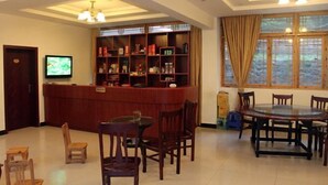 Un vestíbulo de hotel con mostrador de recepción, un televisor, una estantería y un área de comedor con sillas y una mesa.