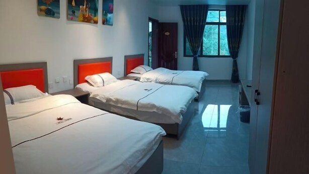 Habitación de hotel con tres camas, una ventana con cortinas y obras de arte en la pared.