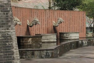 Un muro de piedra con figuras de dragones talladas e inscripciones, un sendero de piedra curvo y una estructura de ladrillo.