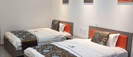 Dos camas individuales con cabeceros naranjas, ropa de cama blanca y almohadones decorativos.