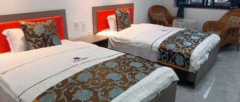 A hotel room with two beds, each with a patterned bedspread and pillows, a small table, and a chair.