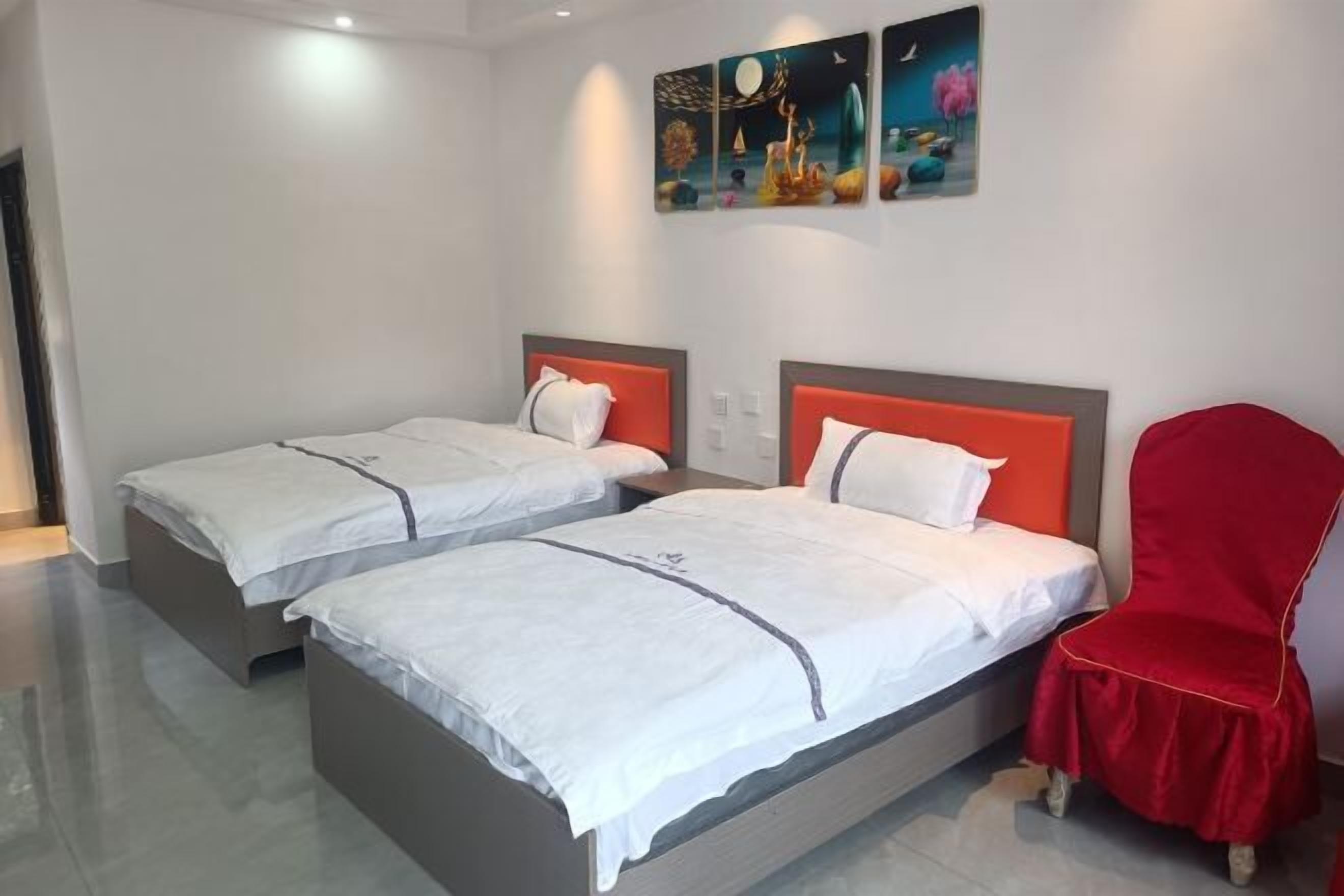 Een hotelkamer met twee bedden, een rode stoel en kunst aan de muur.