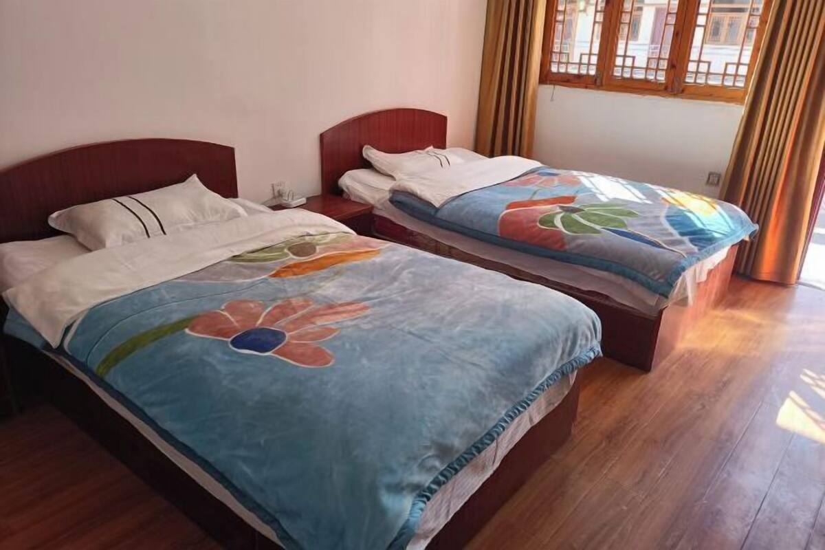 Une chambre avec deux lits, un plancher en bois et une fenêtre avec des rideaux.