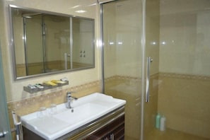 A bathroom with a large mirror, a sink, and a glass-enclosed shower area. - Kangchao Hotel, Yueqing (Yueqing)