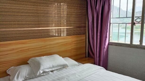A hotel room with a wooden headboard, a bed with white linens, and a view of a lake through a window with purple curtains. - Kangchao Hotel, Yueqing (Yueqing)