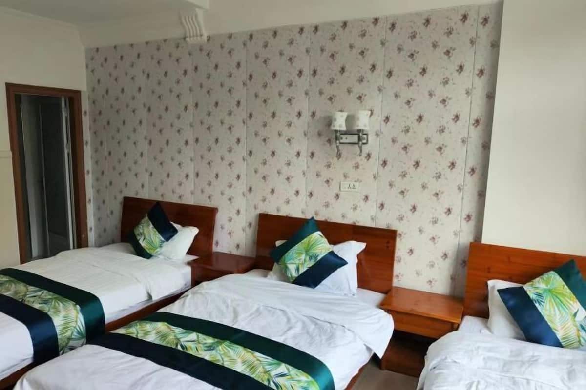 Une chambre d’hôtel avec trois lits simples, une tête de lit en bois, une petite lampe de chevet fixée au mur et un papier peint à motifs floraux.
