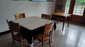 Una habitación con una mesa cuadrada rodeada de cuatro sillas de madera, una mesita de madera y una ventana con cortinas.