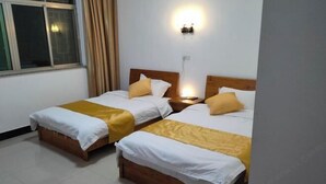 Habitación de hotel con dos camas, una mesita de noche, una lámpara de pared y una ventana con cortinas.