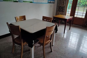 A dining area with a table and chairs, a small table, and a window with curtains. - Living Of Mountain Farmstay (Yushan)