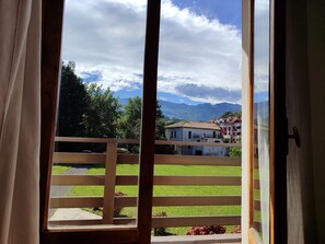 Uma varanda com guarda-corpo de madeira, vista para gramado verde e edifícios ao fundo.