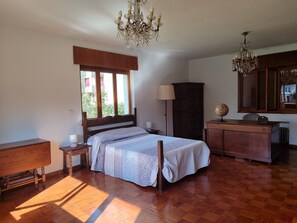 Quarto com piso de madeira, cama com roupa de cama estampada, cômoda, abajur, globo terrestre e lustre.