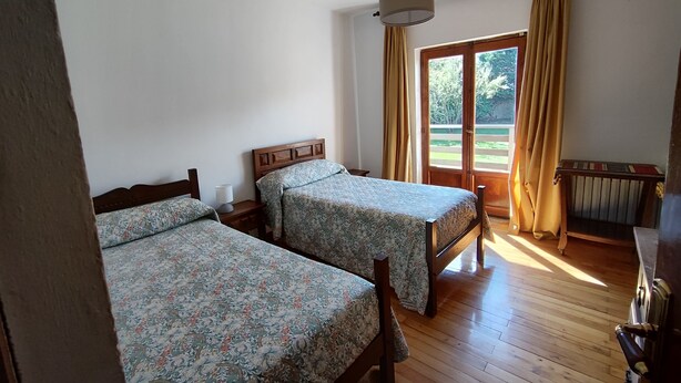 Una habitación con dos camas de madera con ropa de cama estampada, suelo de madera, una ventana con cortinas y un radiador.