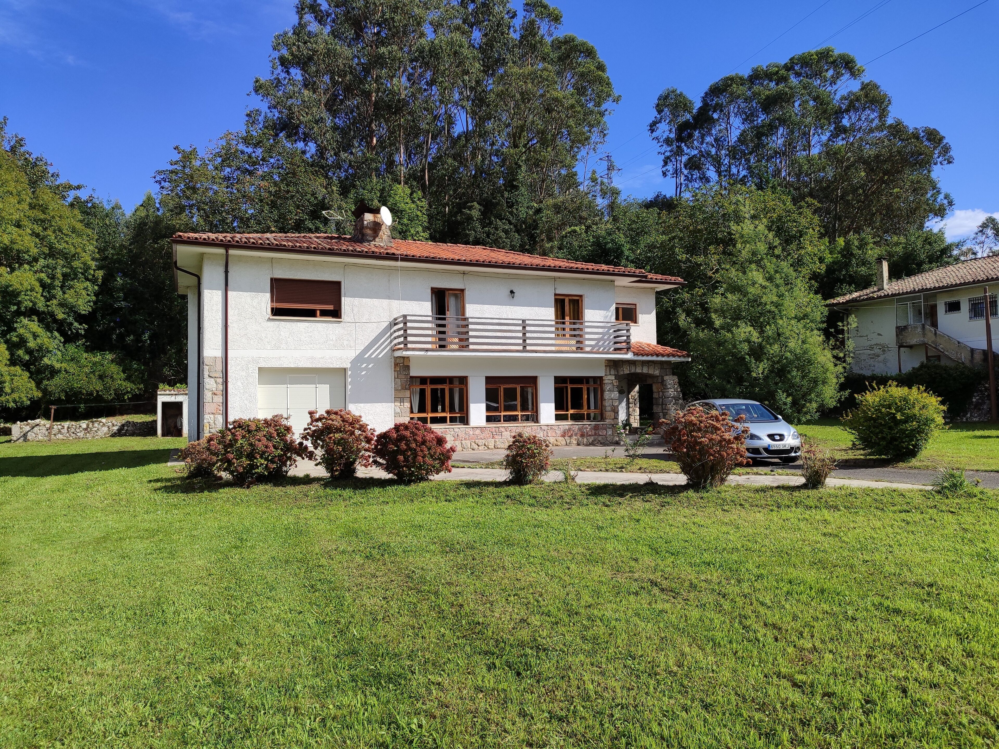 A two-story house with a balcony, a car parked in front, and a well-maintained lawn.
