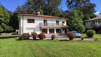 A two-story house with a balcony, a car parked in front, and a well-maintained lawn.