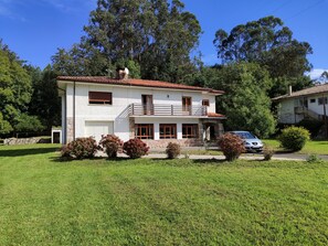 Uma casa de dois andares com varanda, um carro estacionado na frente e um gramado bem cuidado.