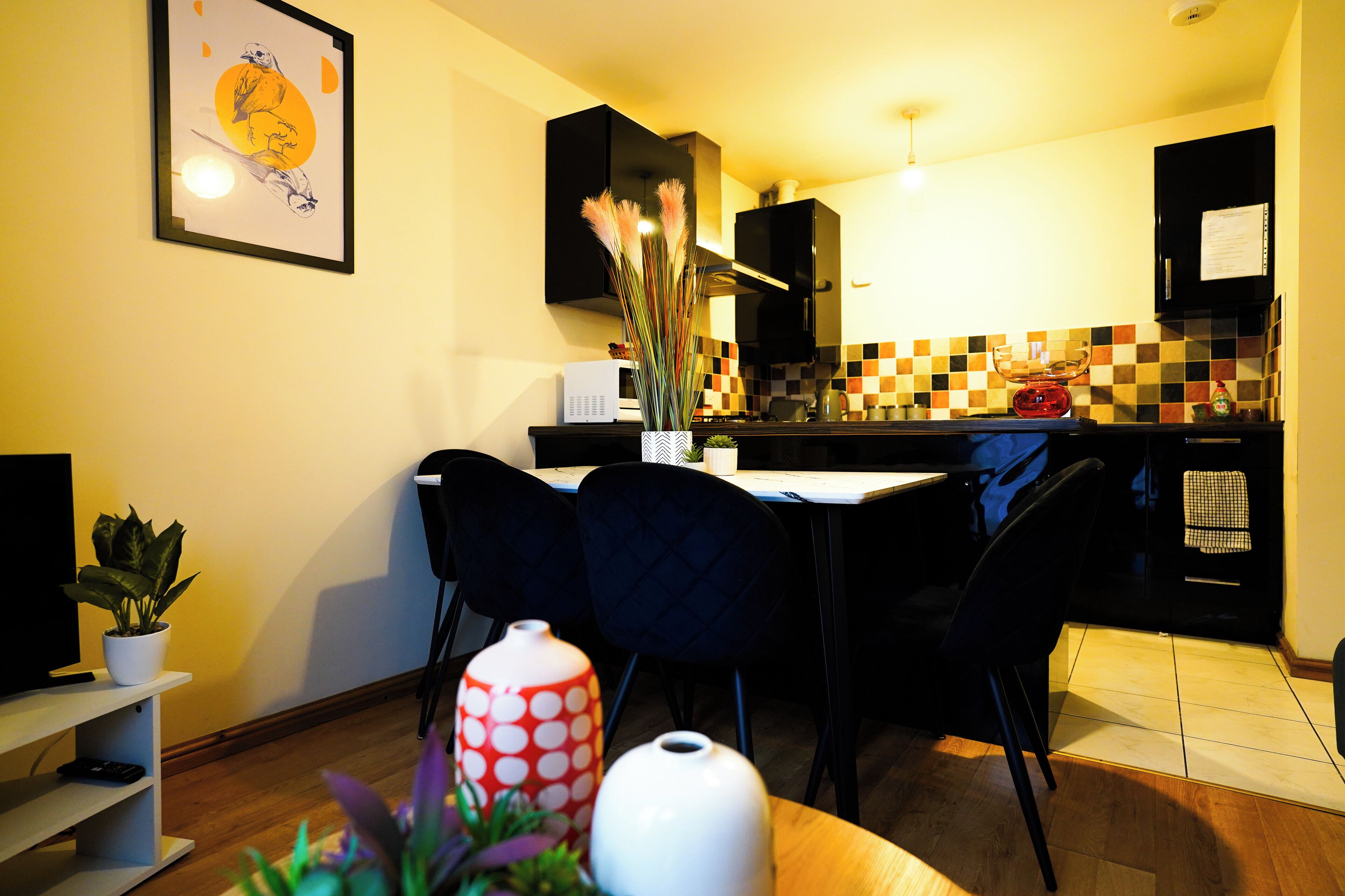 A compact kitchen with a dining area, featuring a microwave, a coffee maker, and a potted plant.