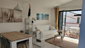 Un soggiorno moderno con un divano bianco, un tavolo da pranzo e una porta vetrata che dà su un patio esterno.