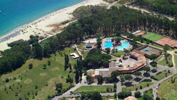Vista aerea di un resort con spiaggia, piscina e campo da tennis.