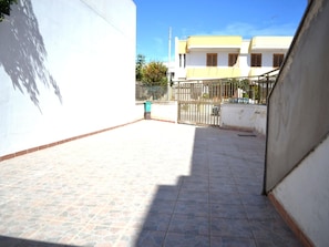 Une cour avec un sol carrelé, une porte en métal et un mur blanc.