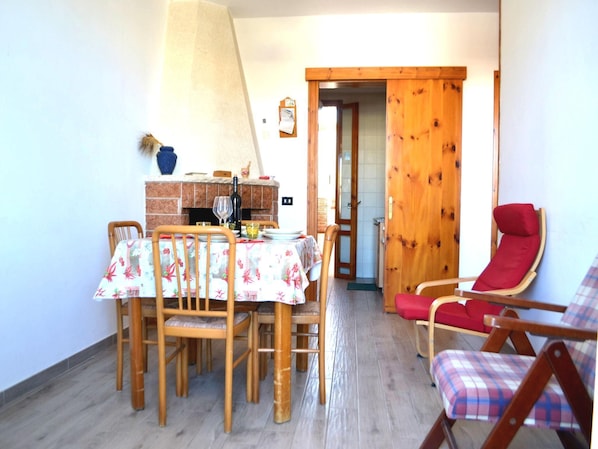 A dining area with a table set for four, a red lounge chair, and a wooden door leading to another room.