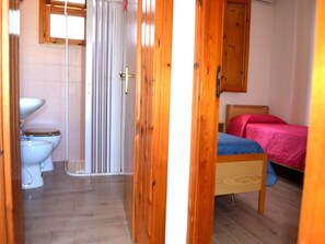 Une salle de bain avec deux toilettes, une douche et un lit en bois recouvert d’une courtepointe rose.