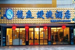 Entrada de hotel con un cartel en caracteres chinos, un número de contacto y farolillos rojos sobre las puertas.